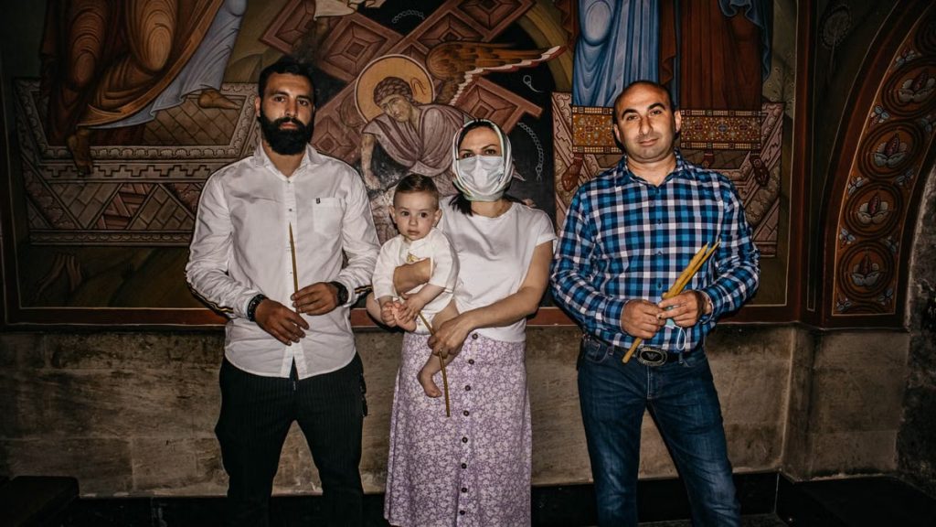A family poses for a photo during a baptism ceremony in a church, highlighting religious tradition.